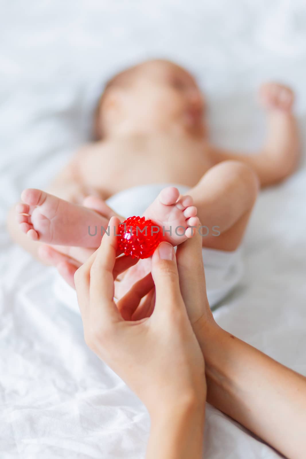 Mother holds newborn baby's feet. Tiny fingers and red massage ball in woman's hand. Cozy morning at home. by aksenovko