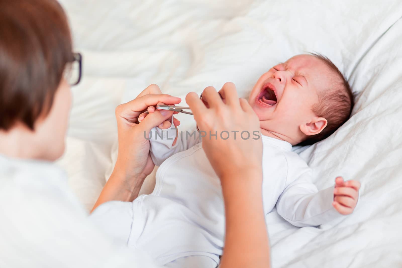 Mother cuts newborn baby's nails with nail scissors. Manicure for little baby.