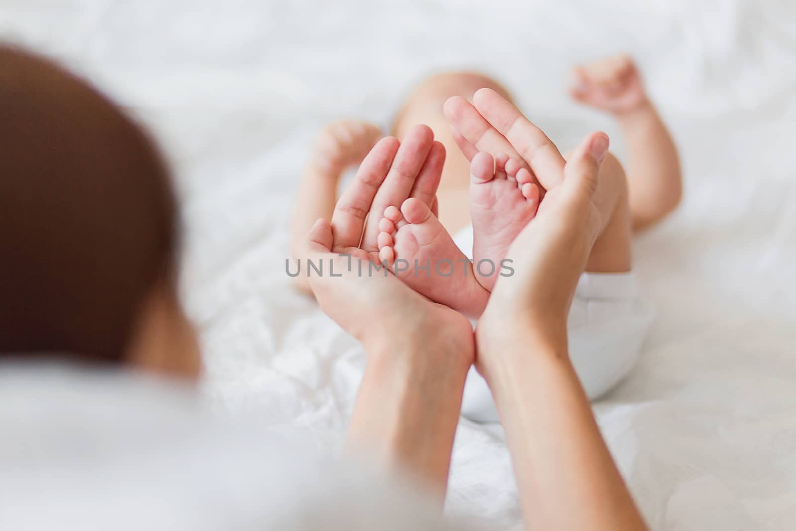 Mother holds newborn baby's bare feet. Tiny feet in woman's hand. Cozy morning at home.