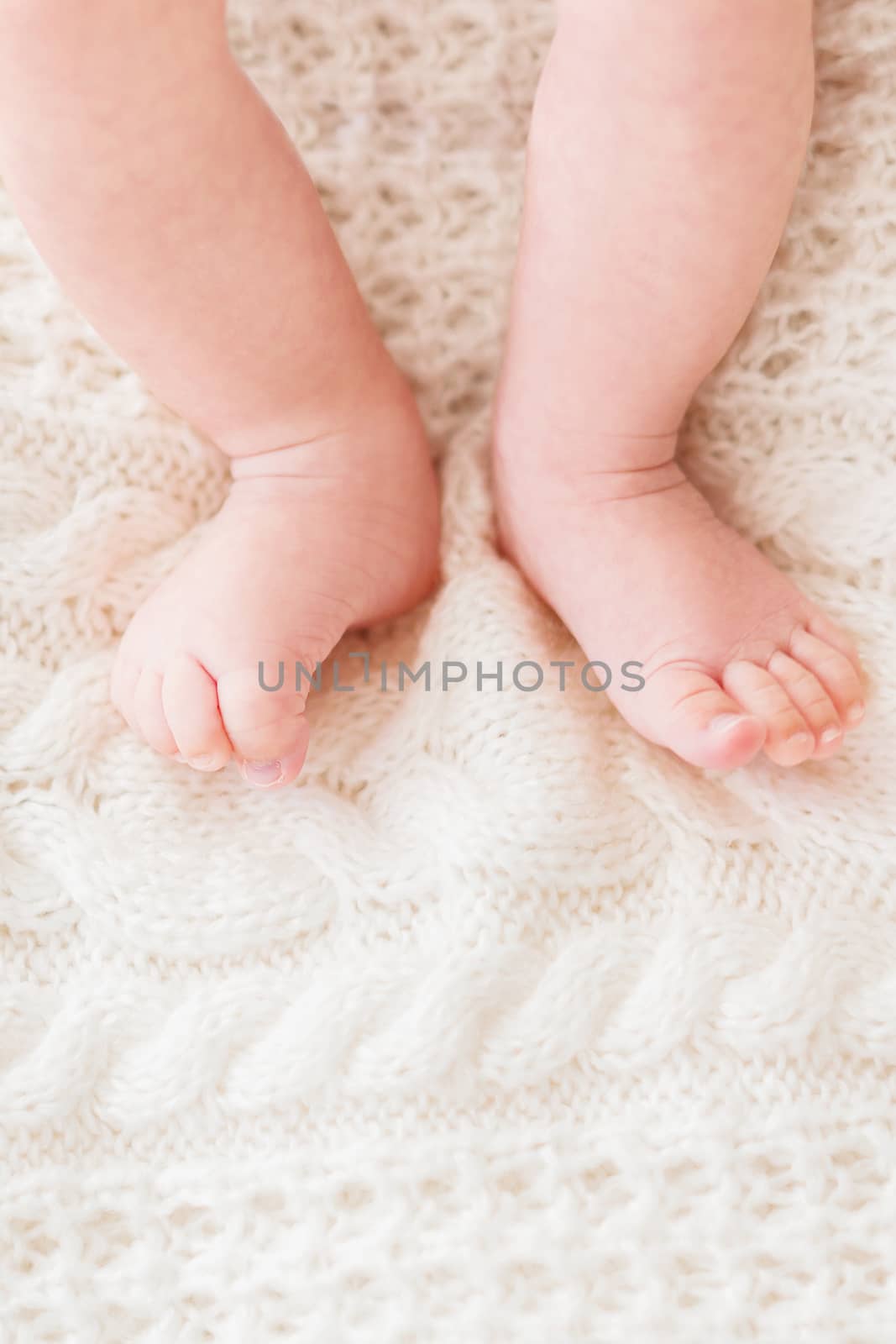 Baby's feet on white knitted background. Little child's bare feet. Cozy morning bedtime at home. Place for text.