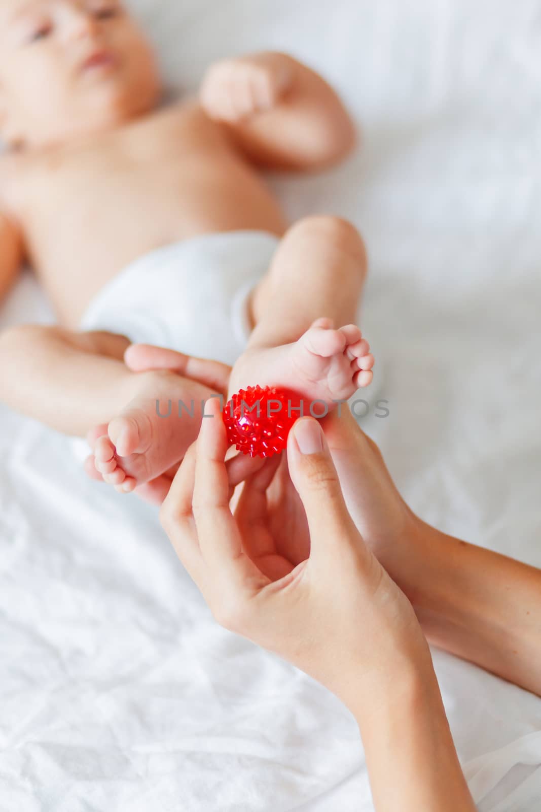 Mother holds newborn baby's feet. Tiny fingers and red massage ball in woman's hand. Cozy morning at home. by aksenovko