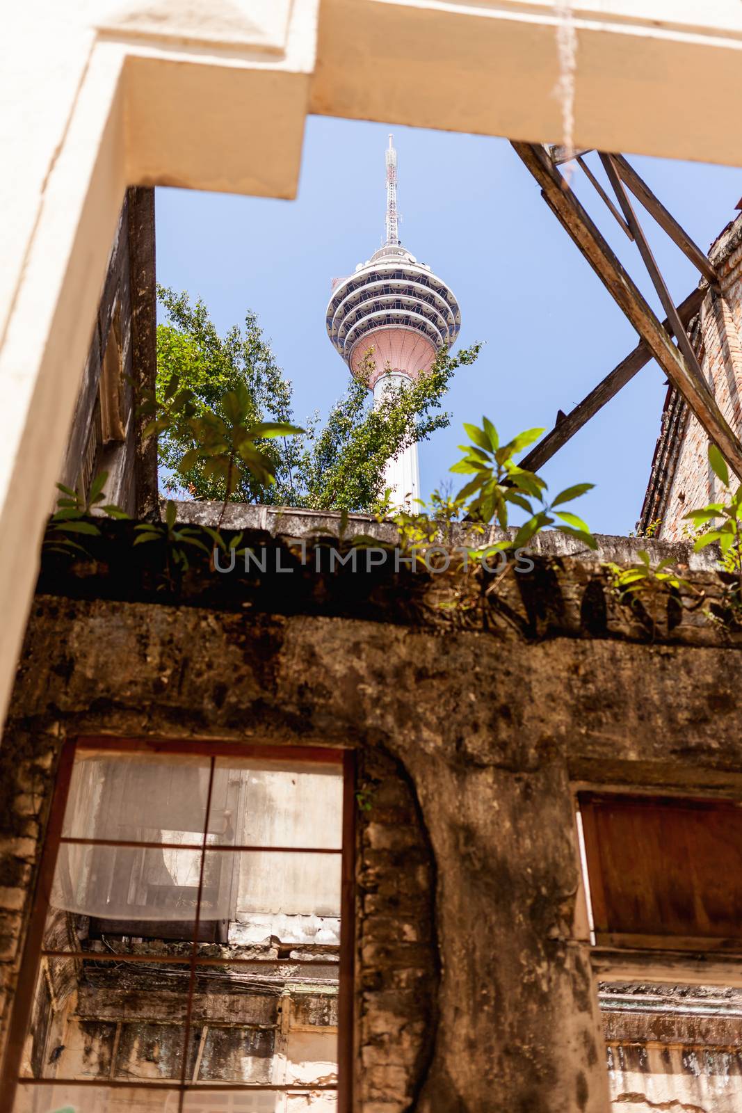 Kuala Lumpur Tower (Menara Kuala Lumpur) is visible through breach in wall of OES building. Old colonial house built in 1931. Kuala Lumpur, Malaysia. by aksenovko