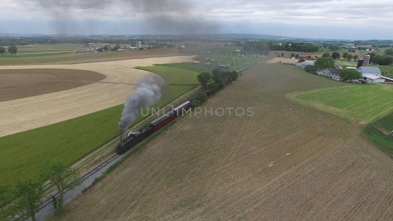 Aerial View of a Steam Passenger Train Puffing Smoke in Amish Countryside on a Sunny Spring Day