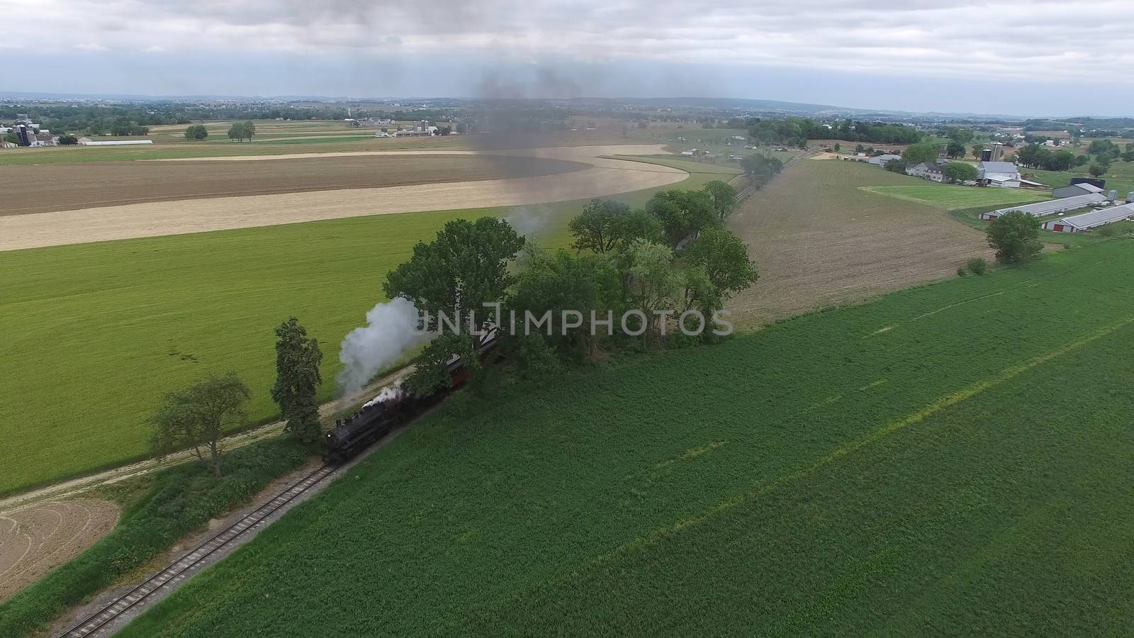 Aerial View of a Steam Passenger Train Puffing Smoke in Amish Countryside on a Sunny Spring Day