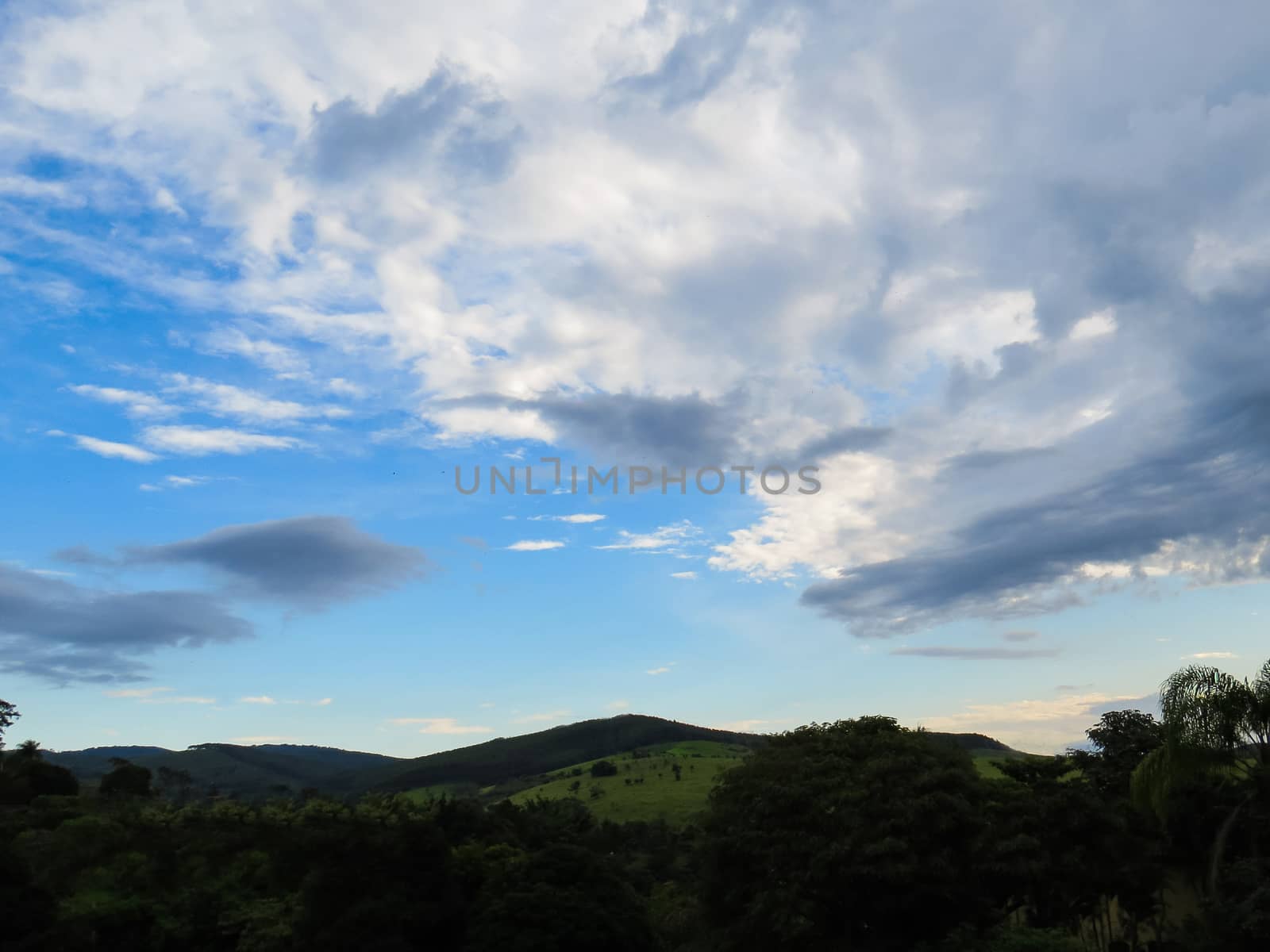 Landscape of sky with clouds in fields at dusk and hills in silhouette.