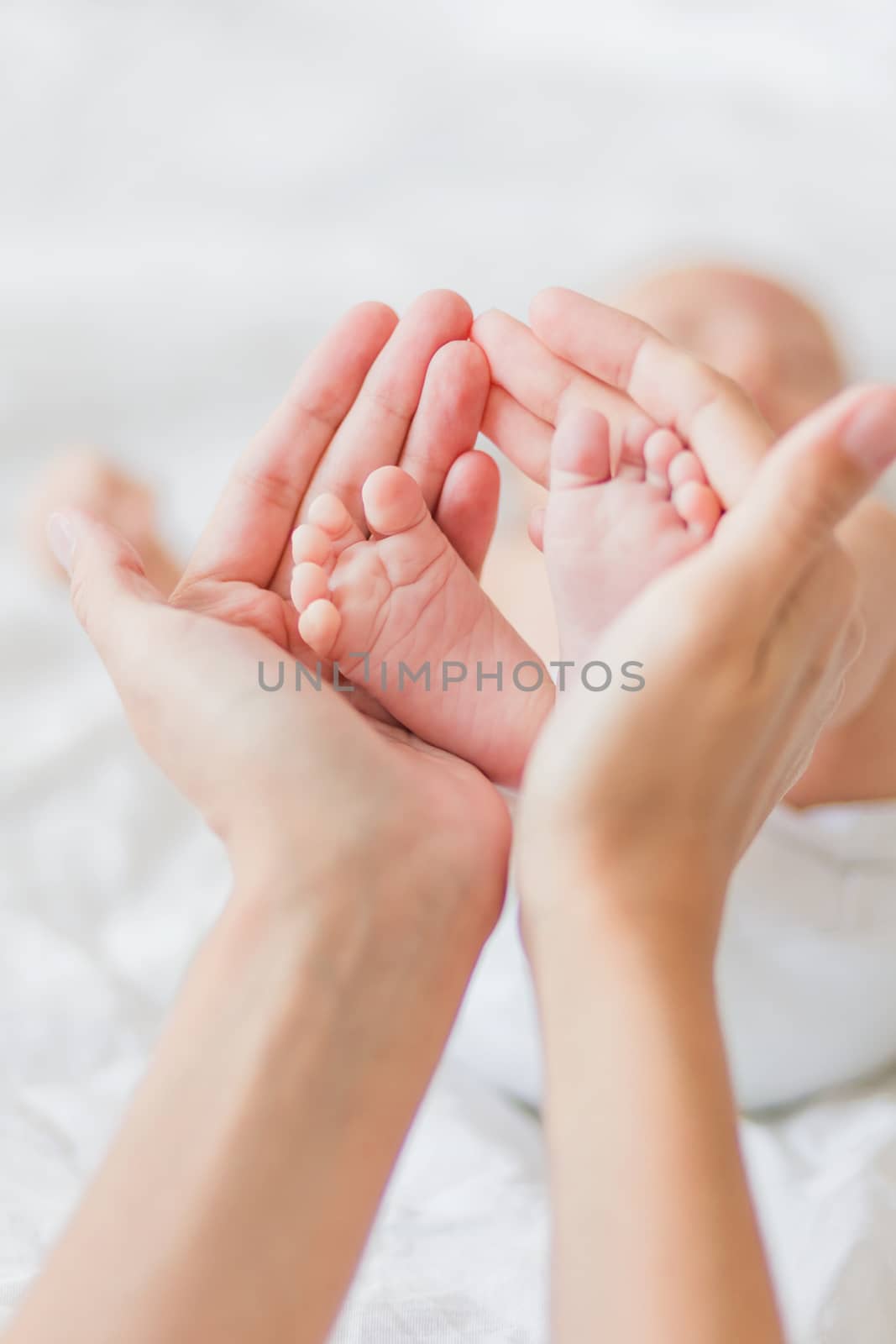 Mother holds newborn baby's bare feet. Tiny feet in woman's hand. Cozy morning at home.