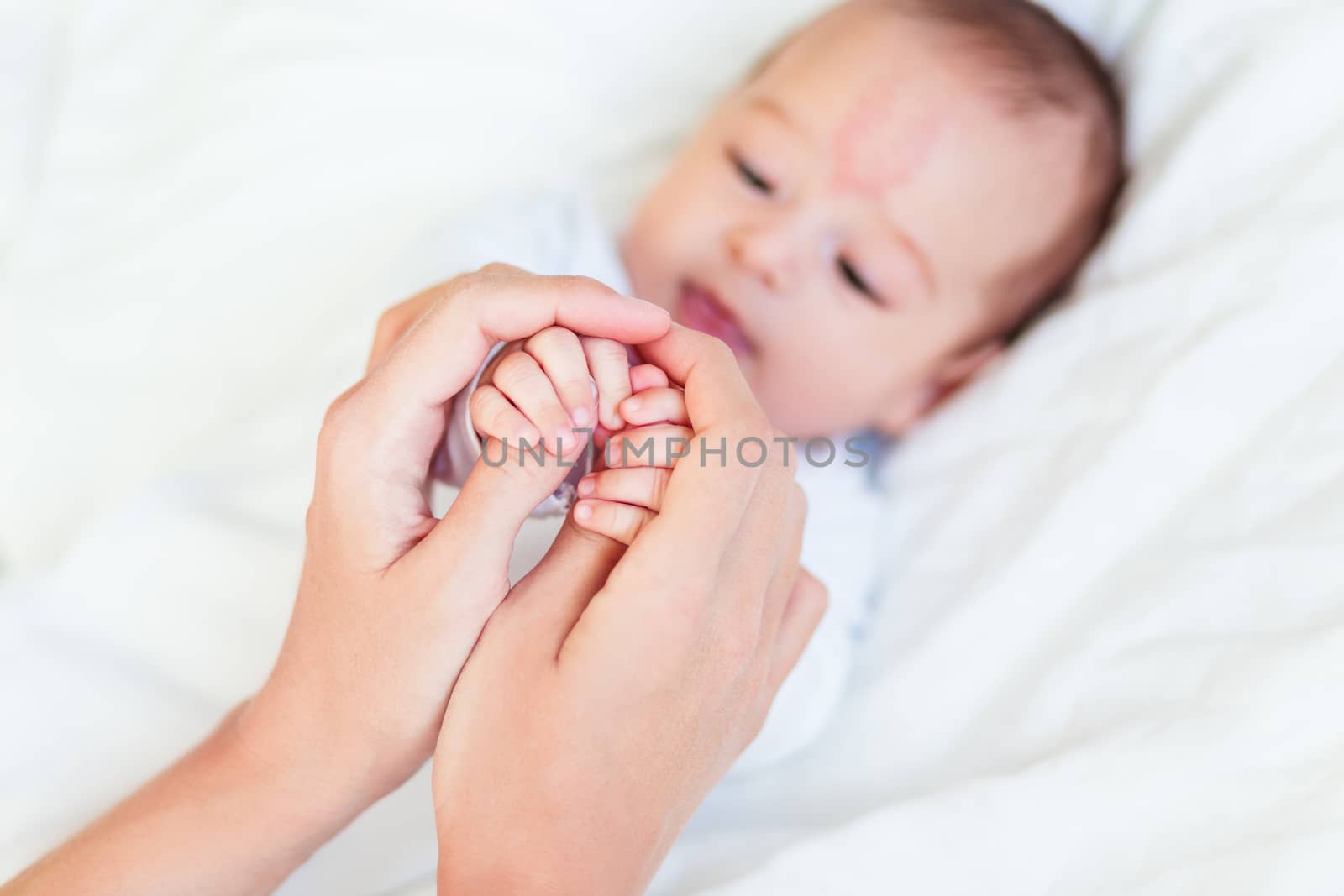 Mother holds newborn baby's hands. Tiny fingers in woman's hand. Cozy morning at home.