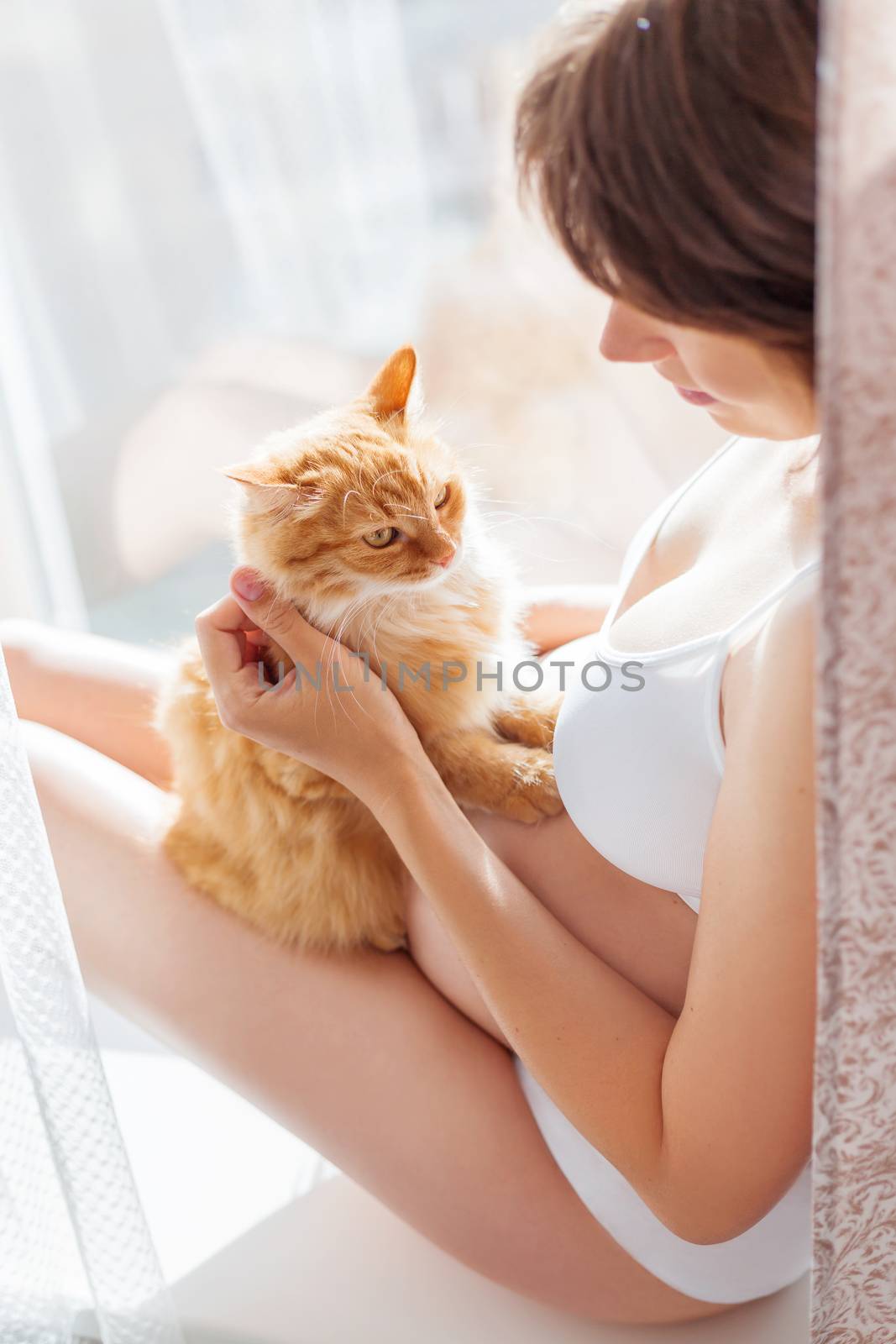 Pregnant woman in white underwear with cute ginger cat. Young wo by aksenovko