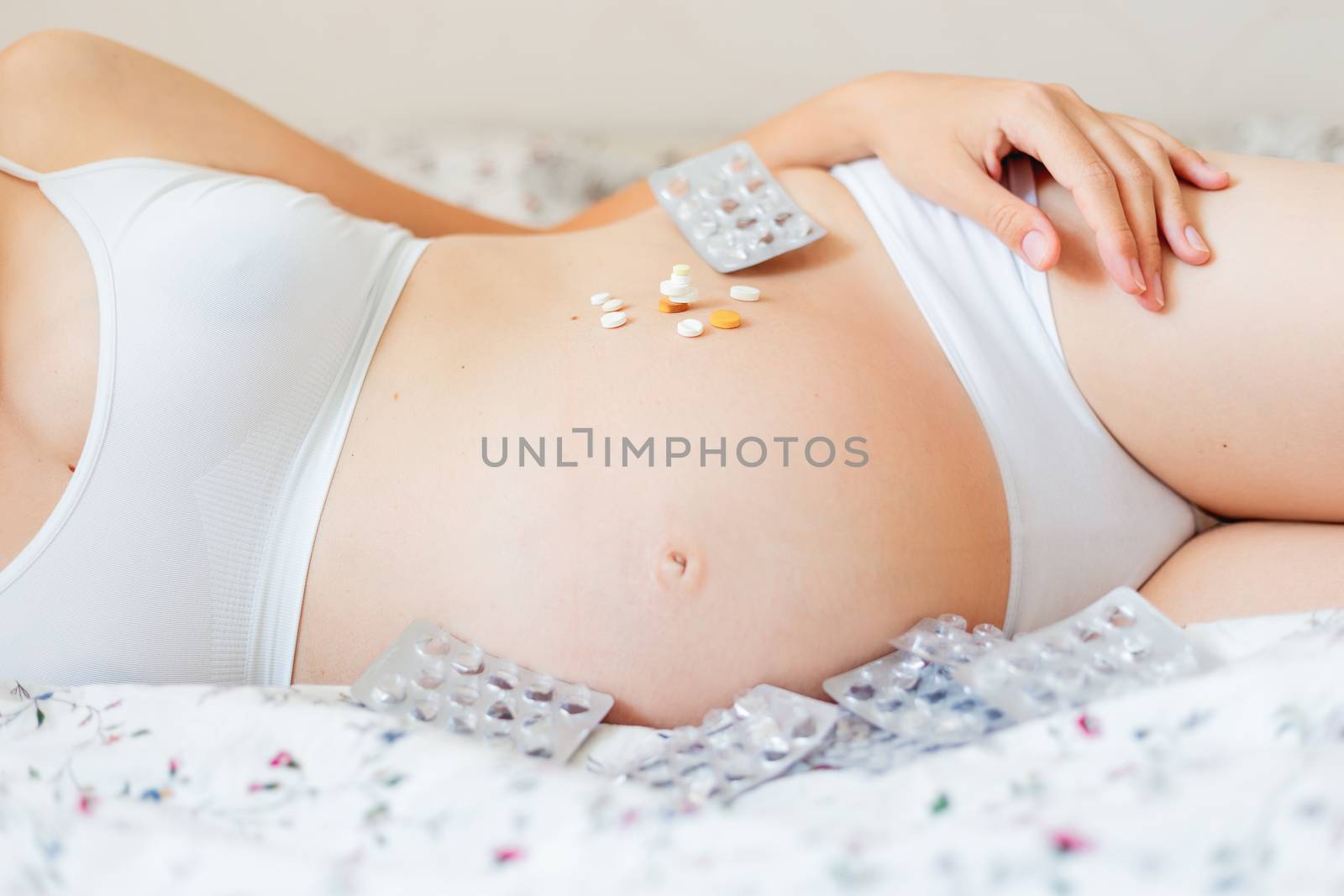 Pregnant woman in white underwear lying in bed with many pills. Young woman expecting a baby and have to take medicine.