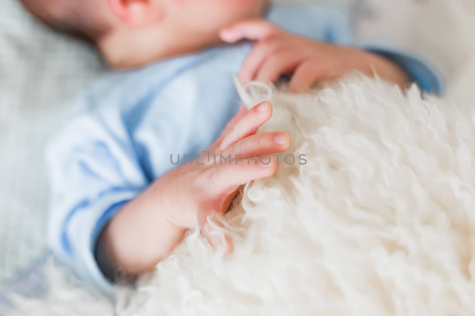 Newborn baby boy palm hand. Tiny fingers with nails. Bedspread made of natural sheep skin.