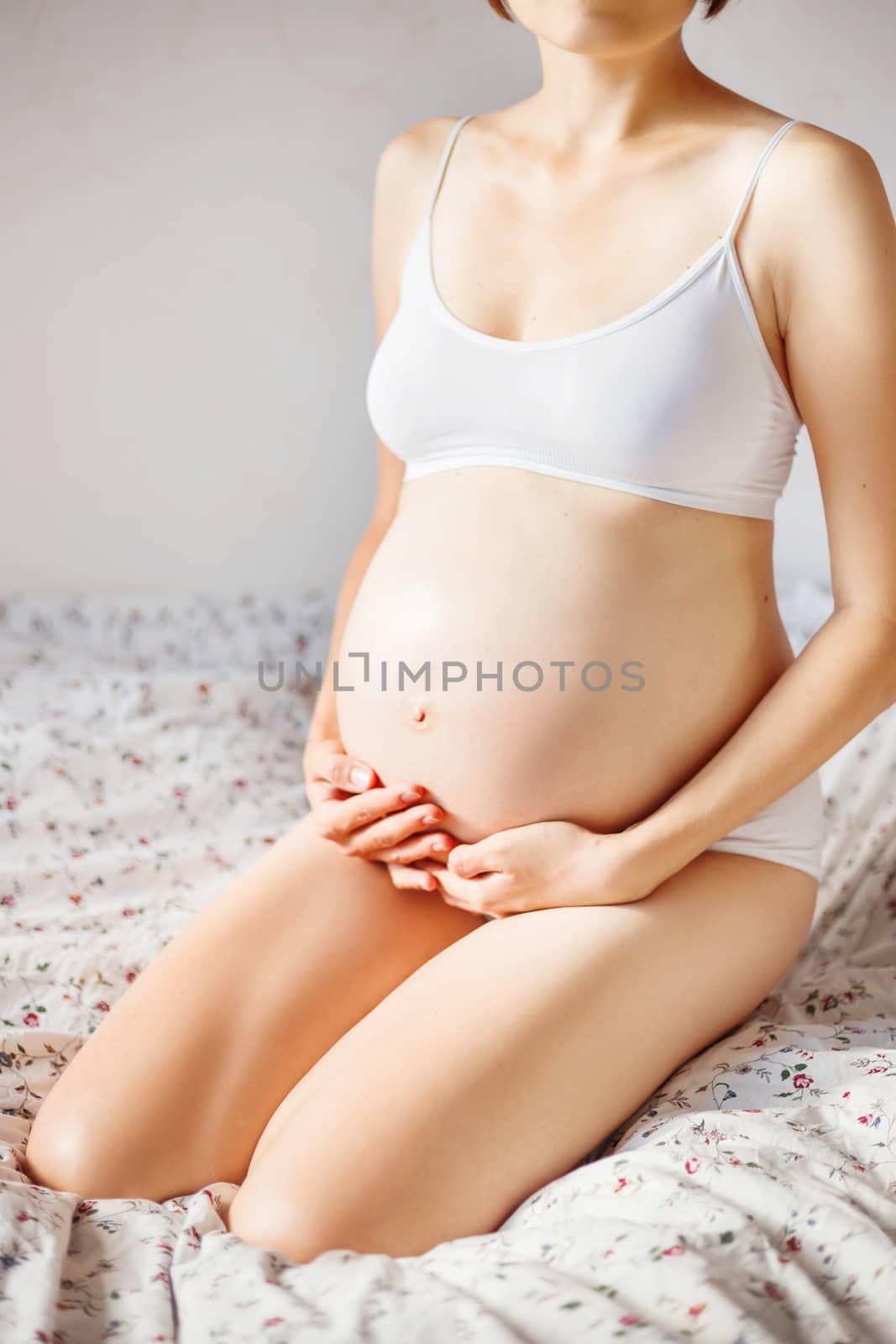 Pregnant woman in white underwear on bed. Young woman expecting a baby.