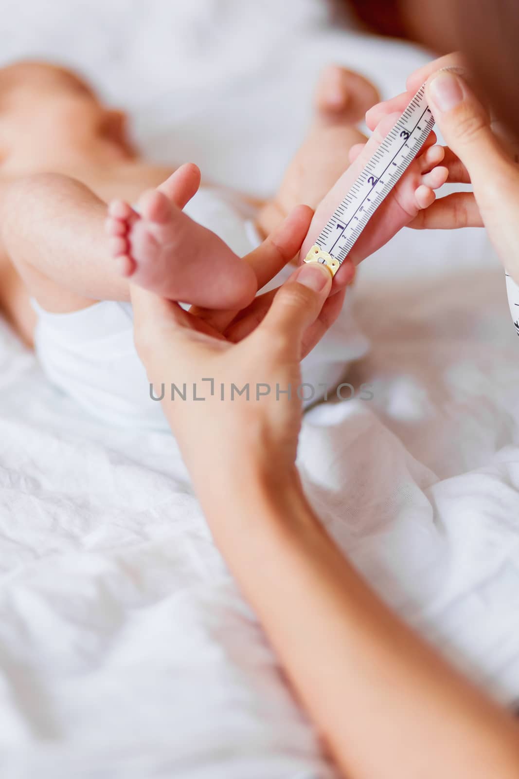 Mother holds newborn baby's bare feet and measures the length of by aksenovko