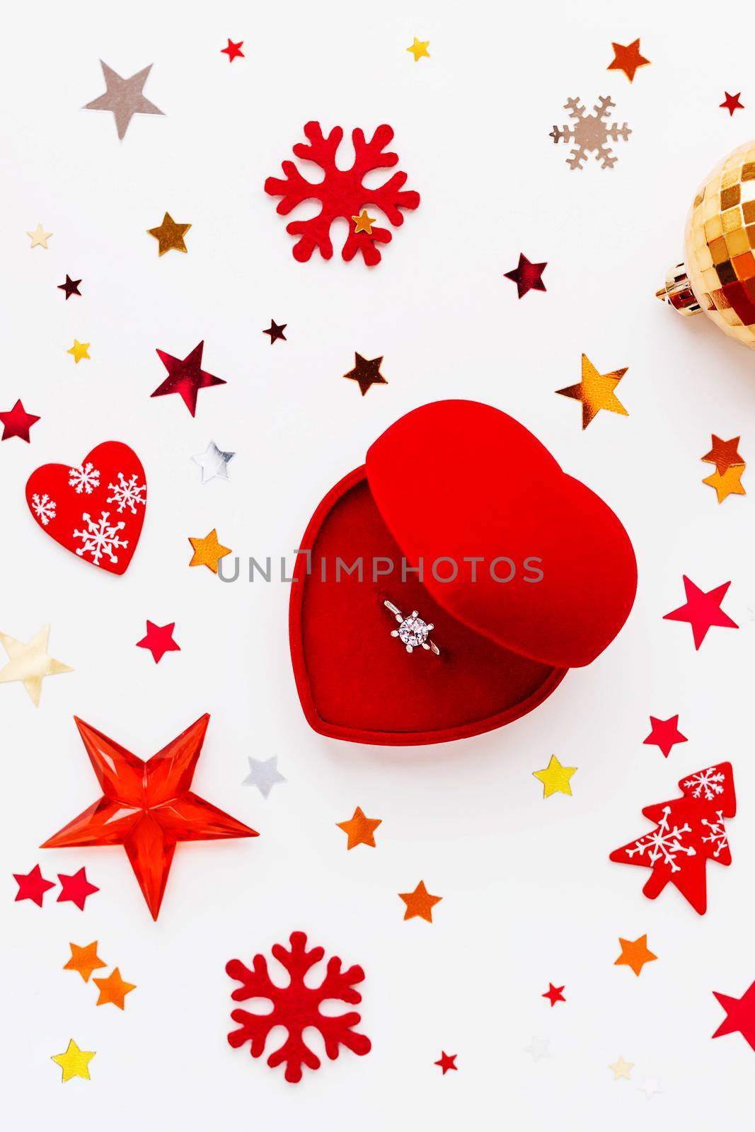 Christmas and New Year holiday background with decorations and engagement ring with diamond in gift heart box. Shiny balls, felt snowflakes and star confetti. Flat lay, top view. by aksenovko