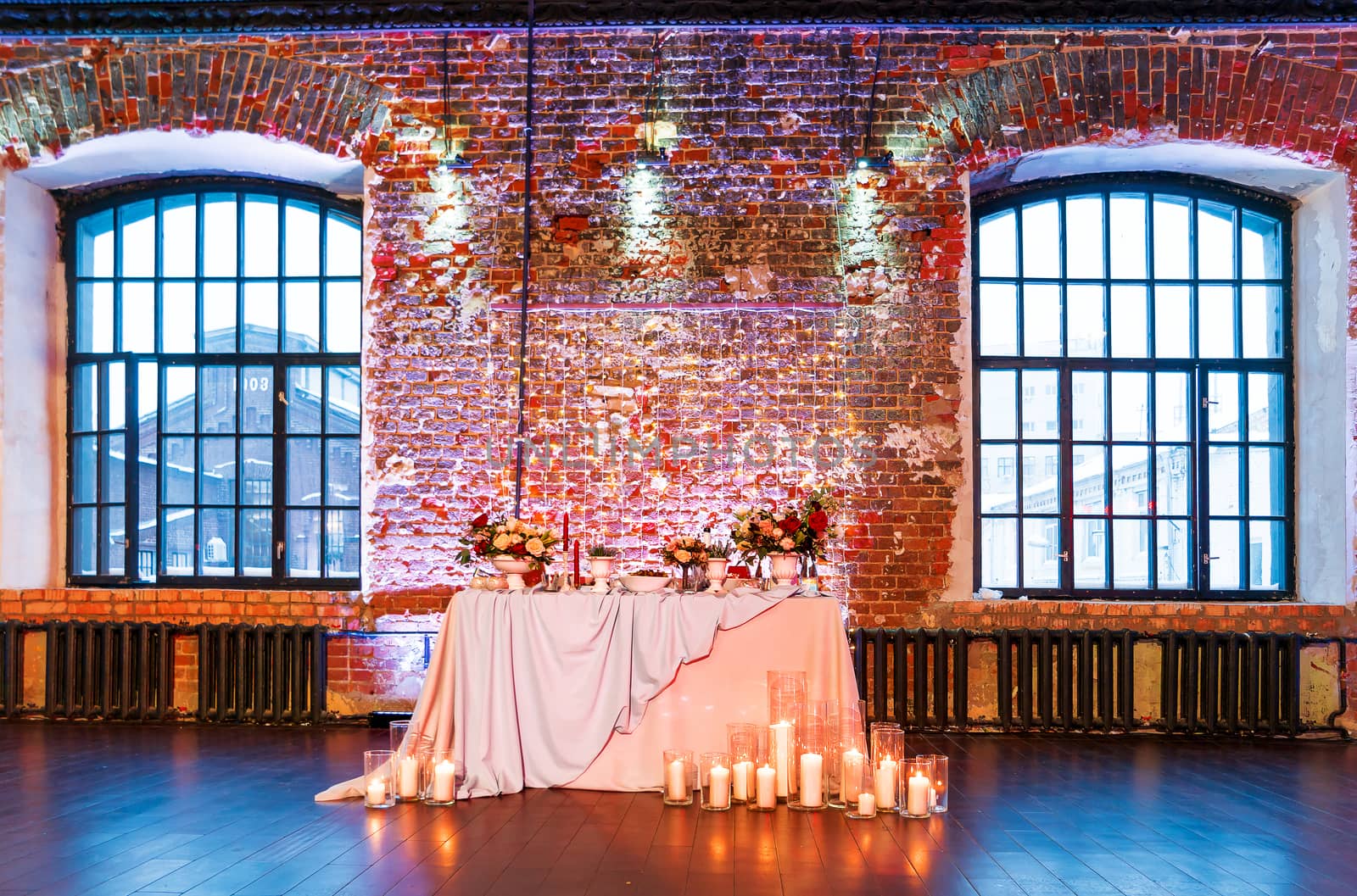 Table set for banquet in loft. Vintage room with brick walls without plaster or wallpapers. Table decorated with candles, fabric and flowers.