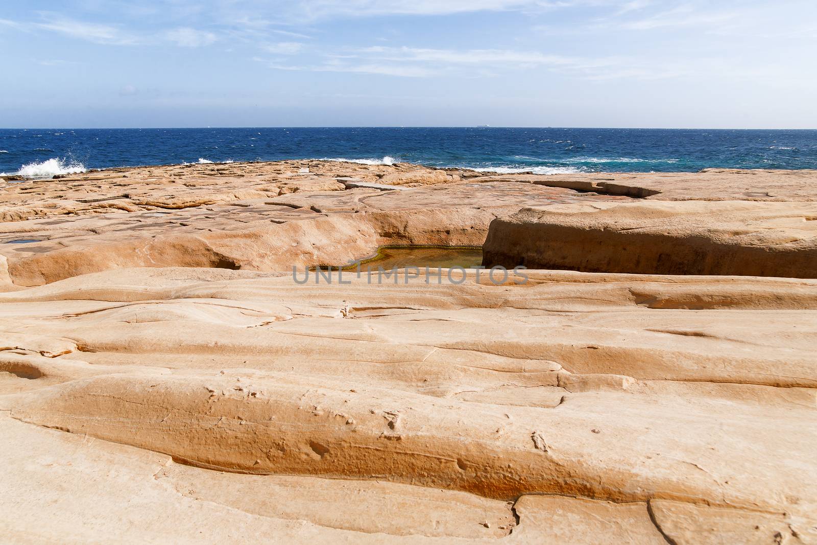 The waves beat against the rocky shore. Water flooded depressions in the rocks. Malta, Saint Julians Bay.