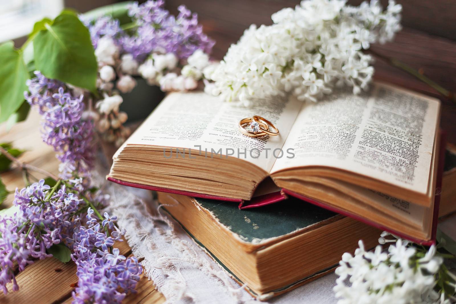 Pair of wedding rings with diamond. Rustic background with old books and lilac flowers. Retro background.
