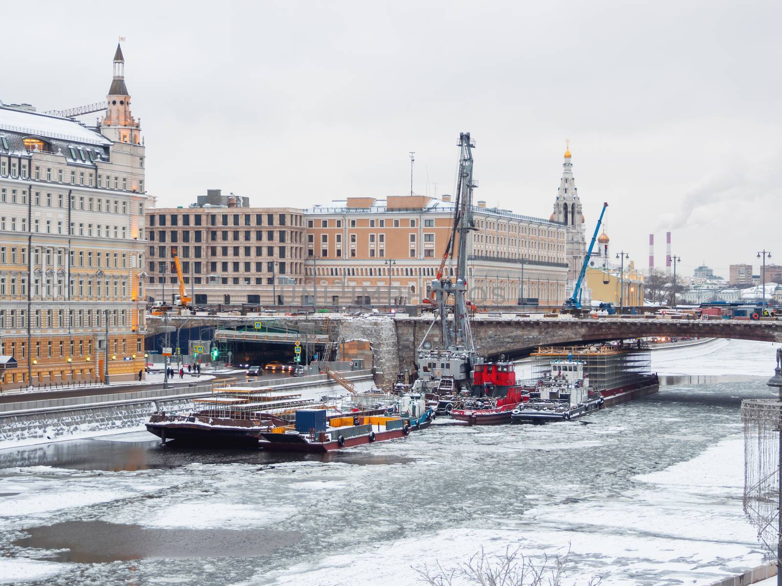 Ships with construction equipment are in Moscow-river under the bridge. Reconstruction of Bolshoy Moskvoretsky Bridge. Winter cloudy day in Moscow, Russia.