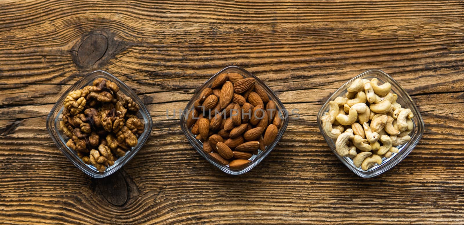 Almond, walnut and cashew in a small plates which standing on a wooden vintage table. Nuts is a healthy vegetarian protein and nutritious food. Nuts on rustic old wood. by vovsht