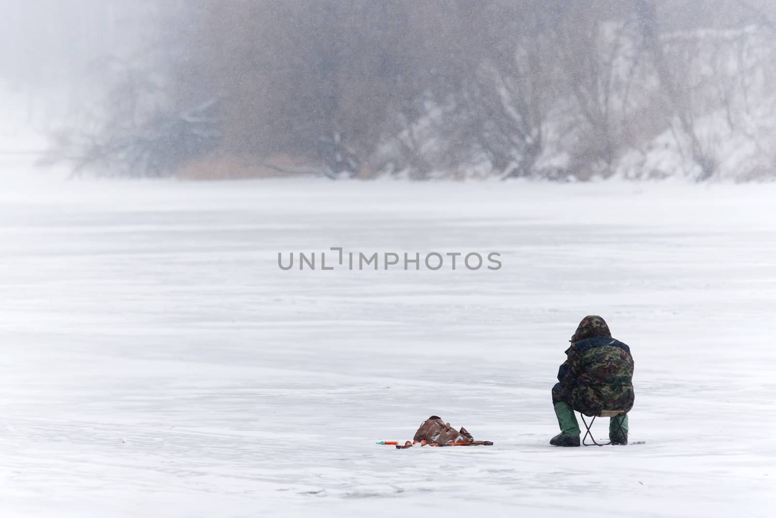 Winter fishing. Man fishes on the ice of a frozen river. Russia.