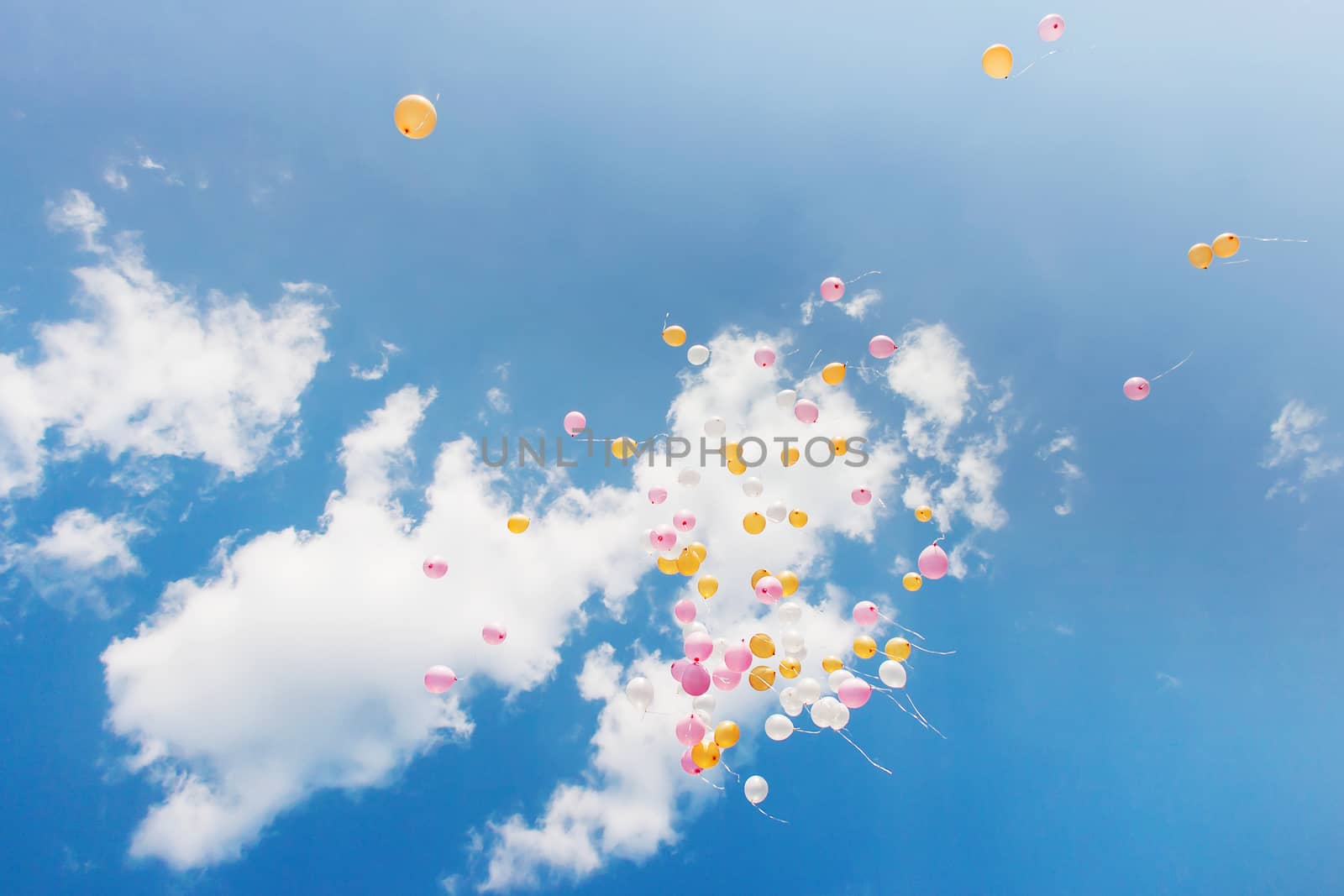 Pink and yellow air balloons fly high in the sky. Sunny day with white fluffy clouds.