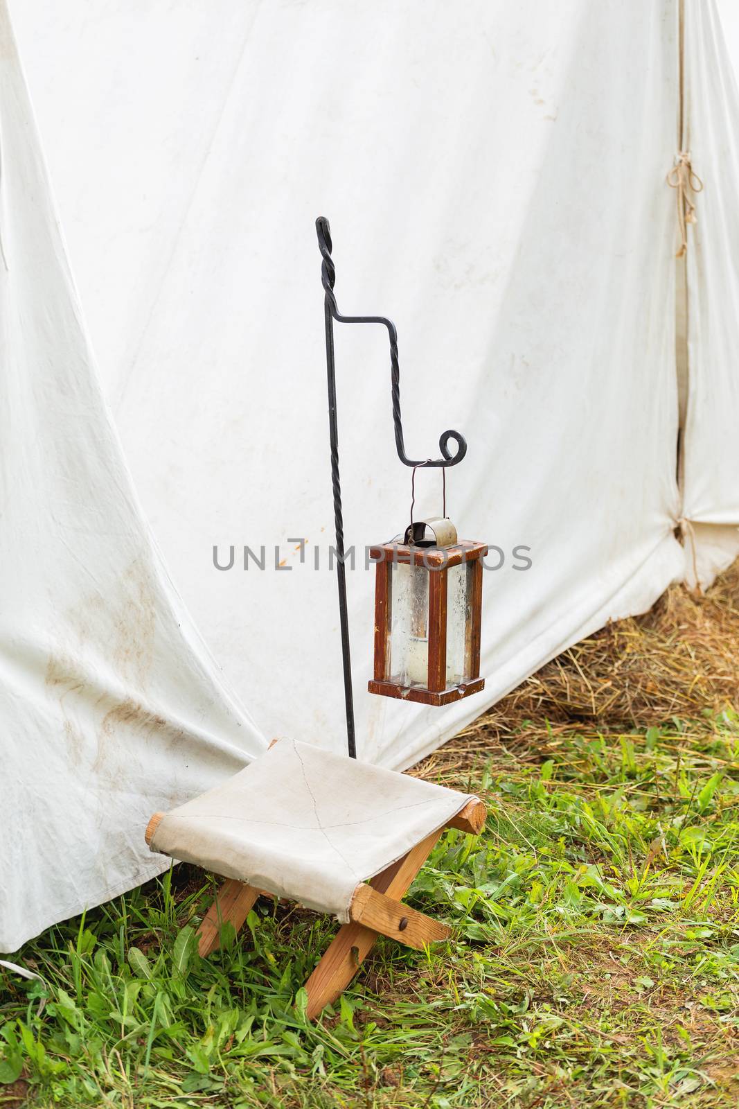 Antique lantern with candle and camp chair at the entrance to the tent. Historical reconstruction of 19th century.