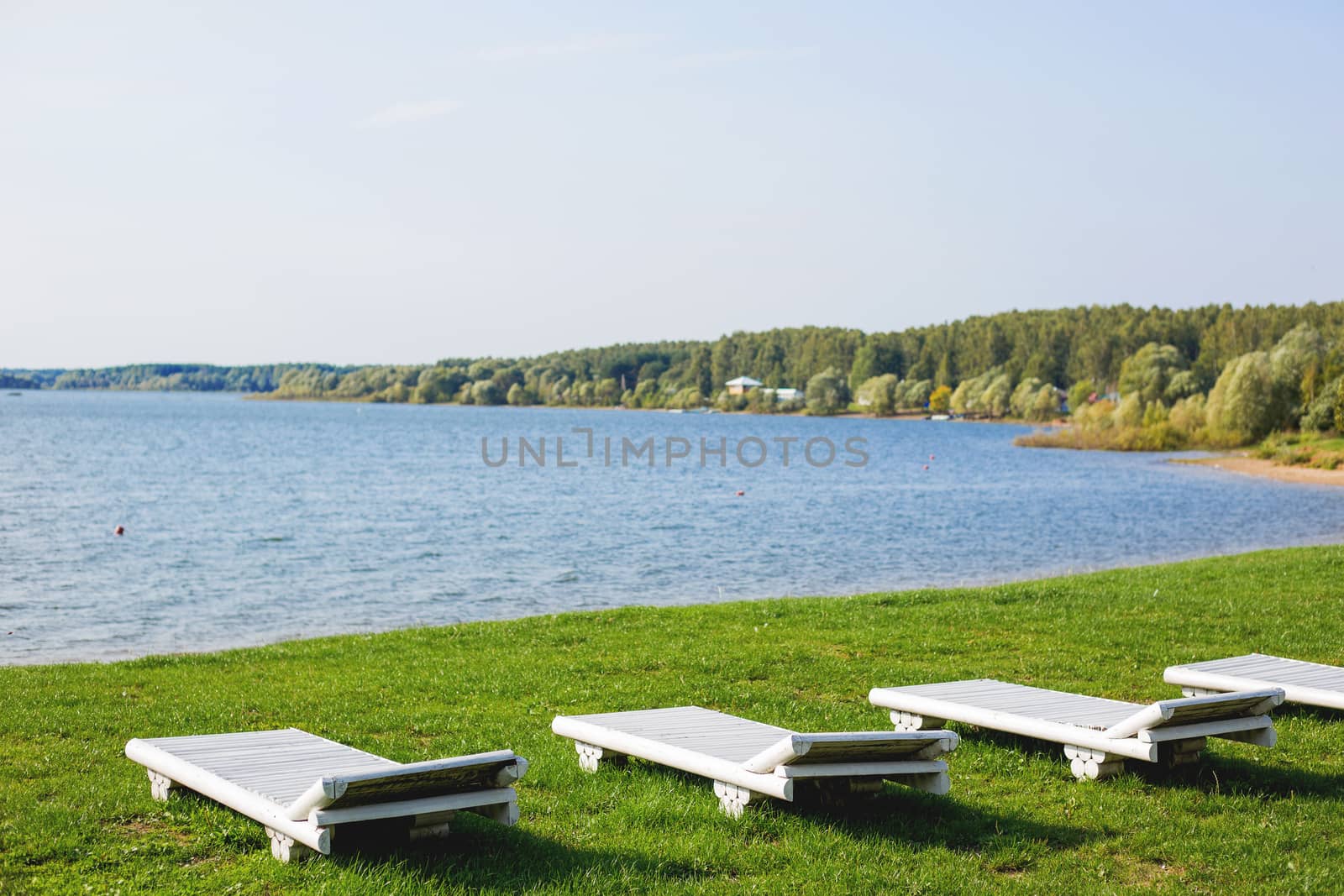 White wooden chaise lounges on the bank of the Ilyinsky reservoir. Outdoor recreation. Moscow region, Russia.