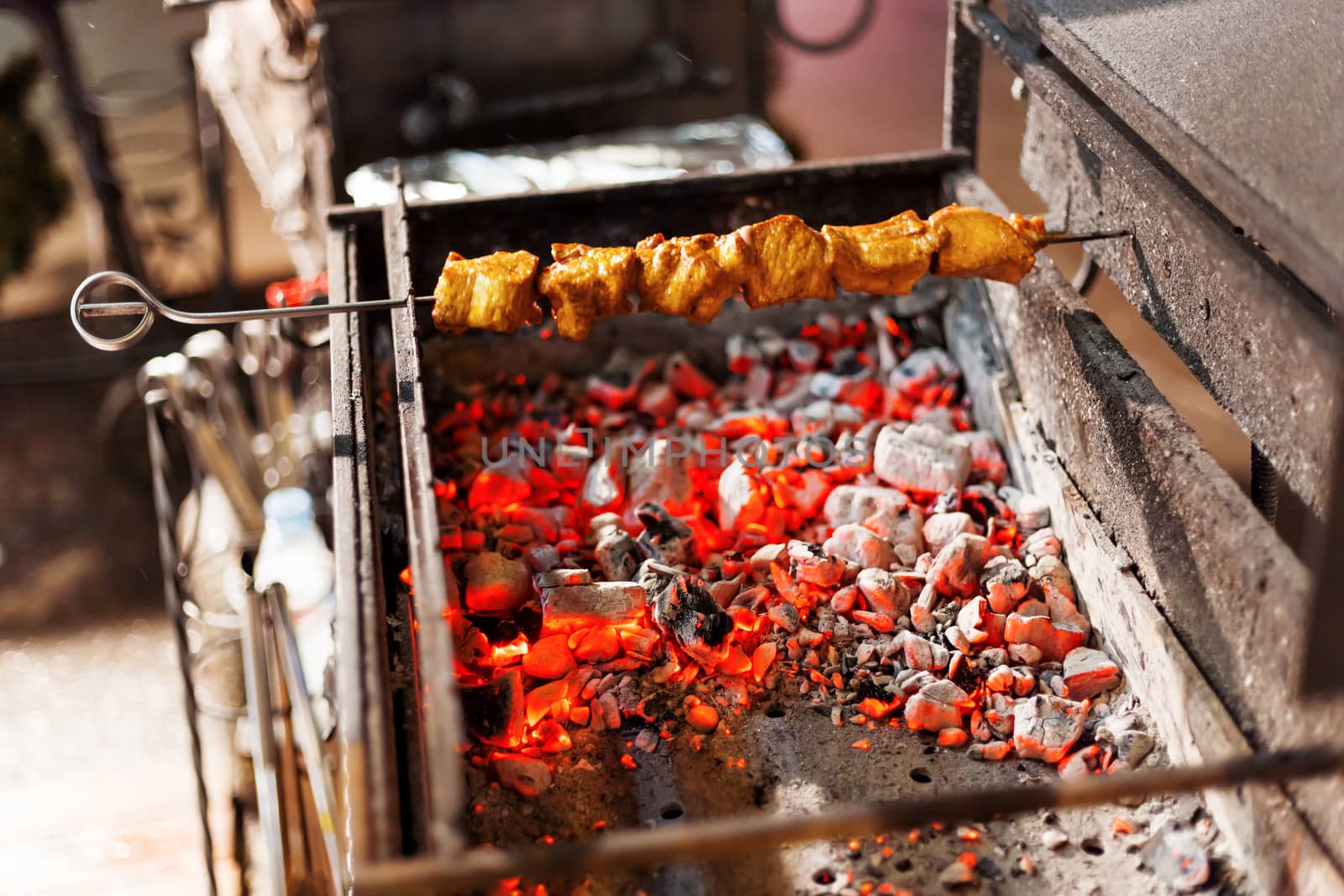 A barbecue skewer spinning on the grill. Fresh steaming meat BBQ. Street cart with grill.
