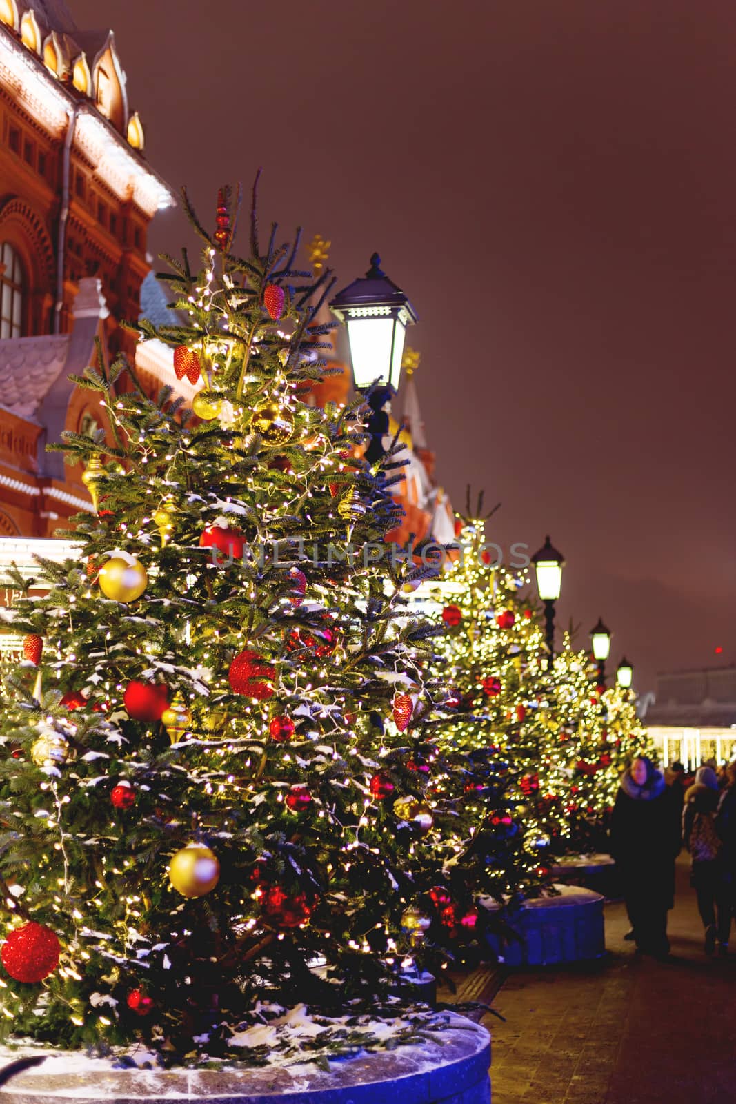 Streets in the historical center of Moscow decorated for New Year and Christmas celebration. Fir trees with bright red and yellow balls and light bulbs. Russia. by aksenovko