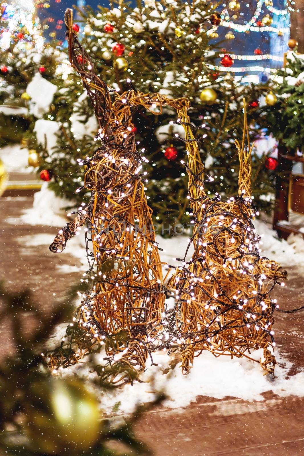 Christmas and New Year background with fir trees and bright decorative bunnies - outdoor decoration made of willow branches with light bulbs garland.