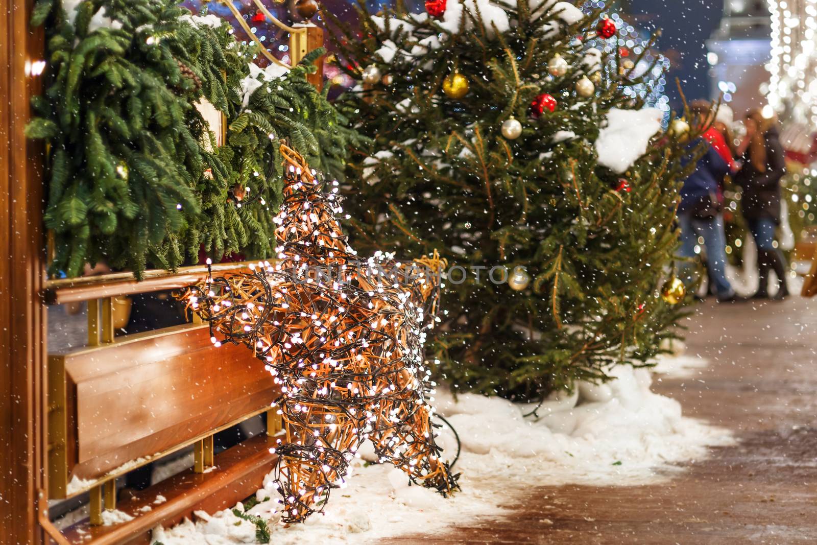 Christmas and New Year background with fir trees and bright decorative star - outdoor decoration made of willow branches with light bulbs garland.