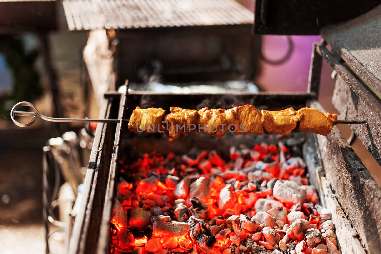 A barbecue skewer spinning on the grill. Fresh steaming meat BBQ. Street cart with grill.