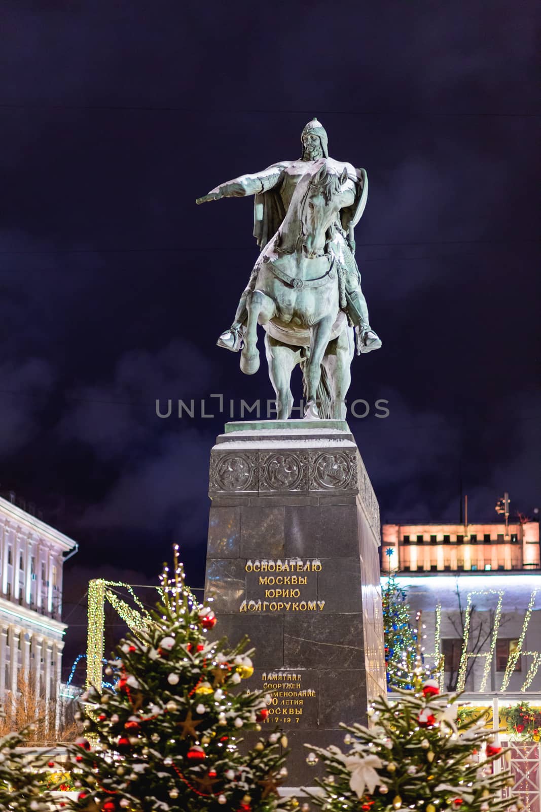 Monument to prince Yury Dolgorukiy, the founder of Moscow, on Tverskaya square (text on pedestal). Street decorated with light bulbs for New Year and Christmas celebration. Russia.
