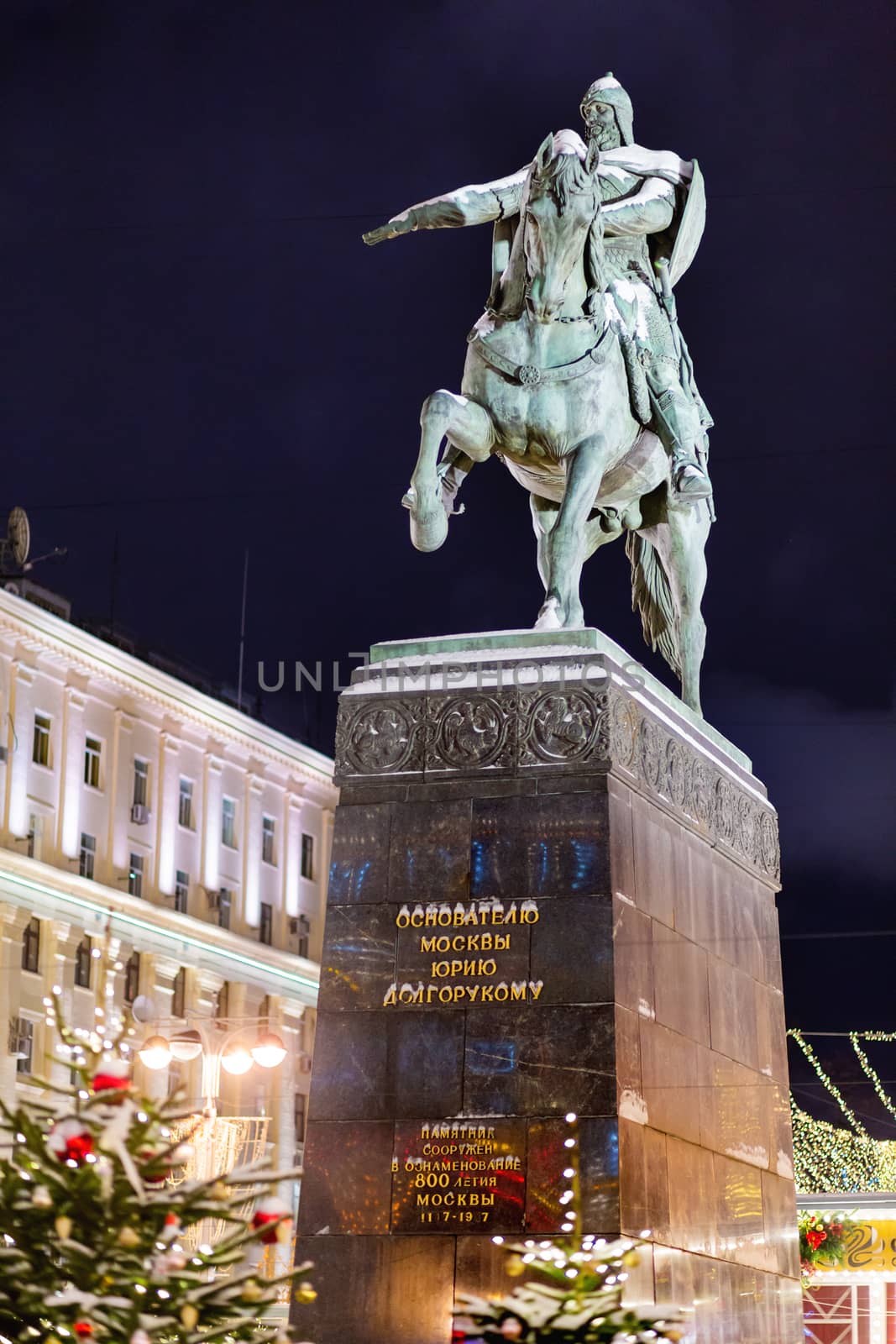 Monument to prince Yury Dolgorukiy, the founder of Moscow, on Tverskaya square (text on pedestal). Street decorated with light bulbs for New Year and Christmas celebration. Russia. by aksenovko