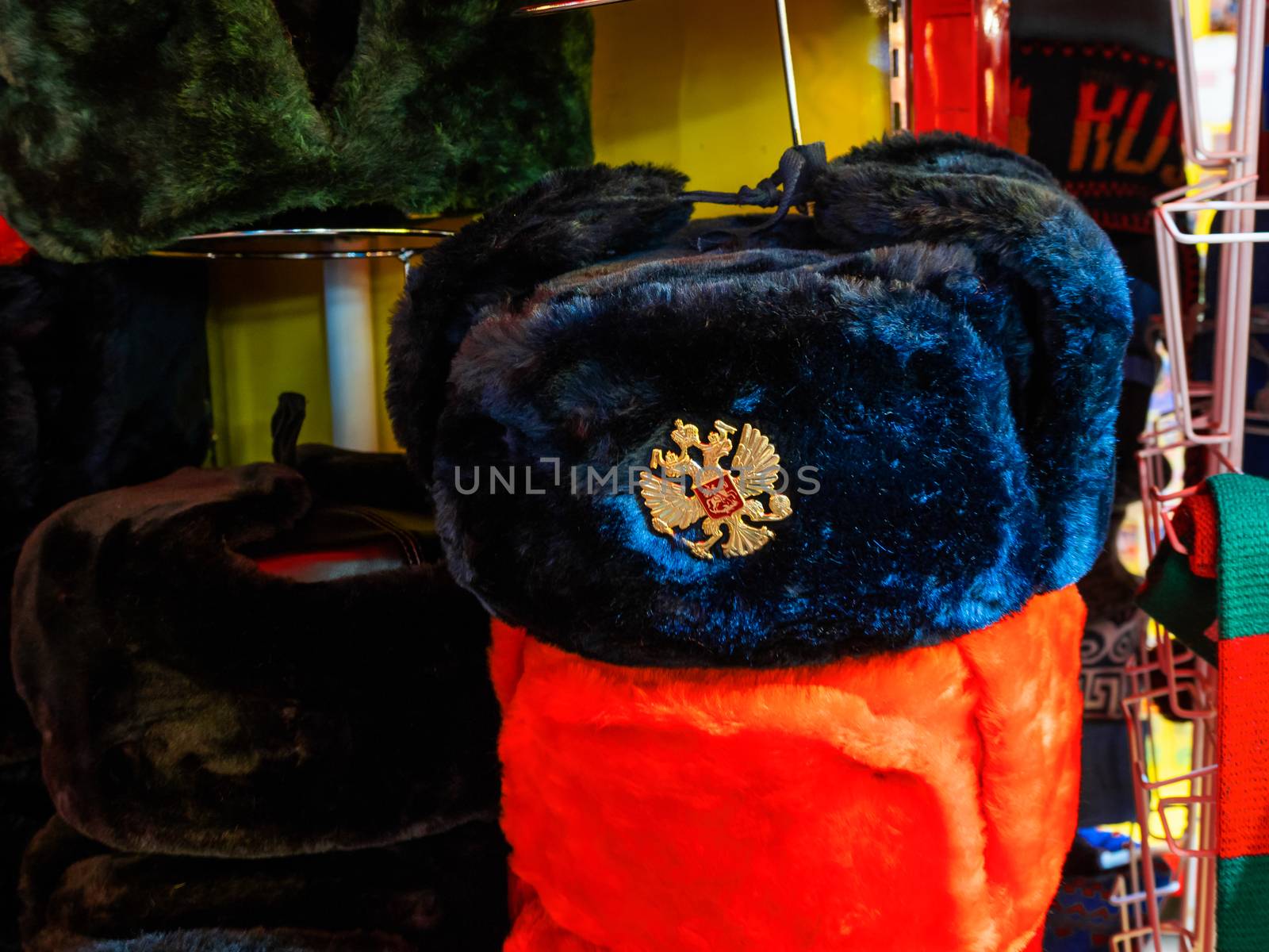 Colorful Russian winter hats with earflaps. Metal pin with Russian double-headed eagle symbol. Souvenir shop in Moscow, Russia.