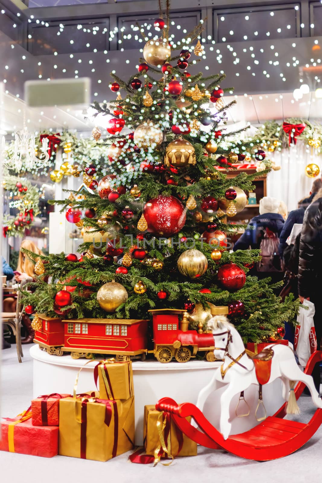 Christmas tree with colorful decorative balls. New Year decorations and gifts - rocking horse, presents ni red and gold wrapping paper. Festive interior of a shop. by aksenovko