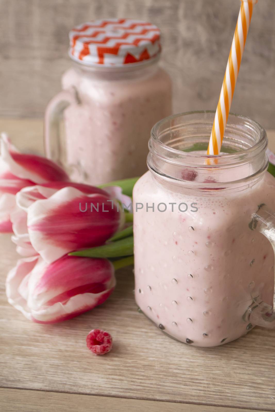 Pink raspberry cream smoothie in mason jar and tulips, vertical