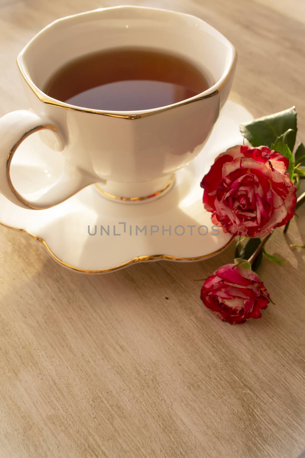 Cup of tea in a china cup and saucer, on a distressed table and roses