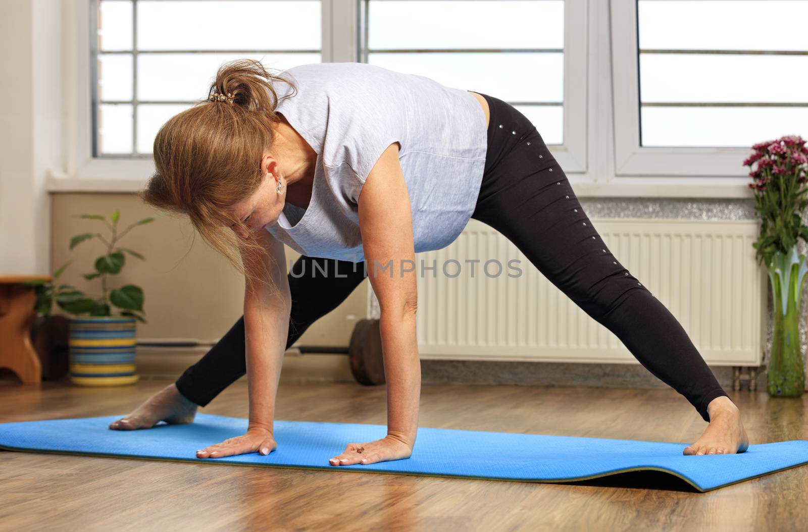 Middle aged or mature woman doing yoga indoors by Sergii
