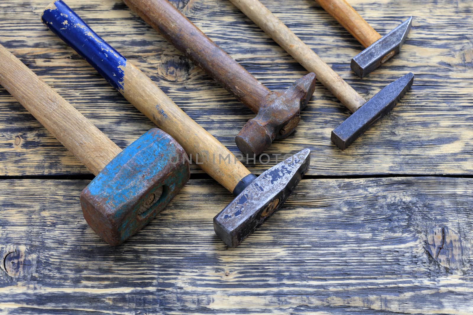 Old worn iron hammers with wooden handles lie on a wooden table.