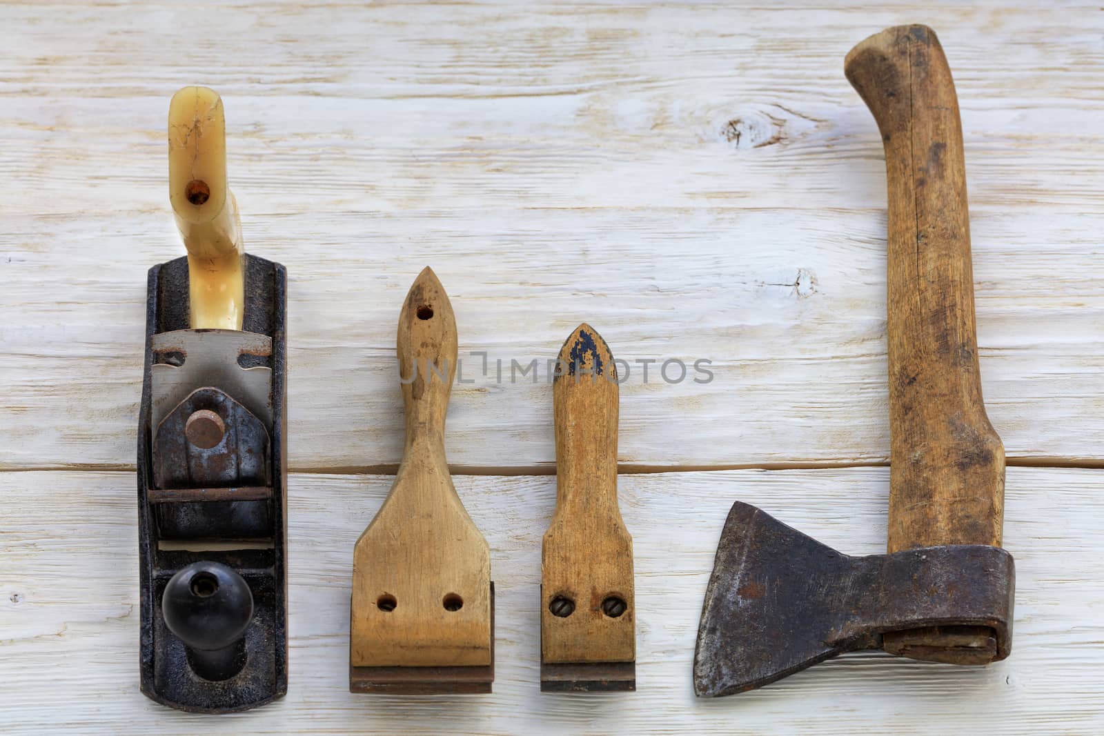 Old carpentry tools, planers, cycles and an ax lie on a white wooden table.