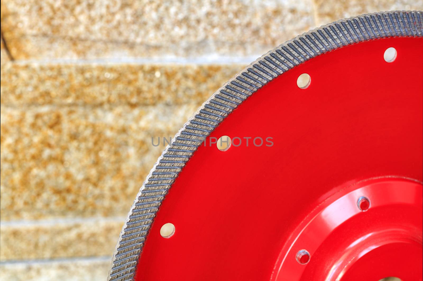 Fragment of a red diamond blade for cutting granite and stone against a background of a wall of golden sandstone. by Sergii