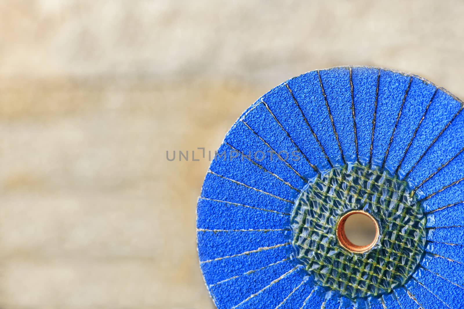 A part of a petal grinding wheel of blue color for sanding wood and rusty metal on a light beige background in unsharpness, close-up.