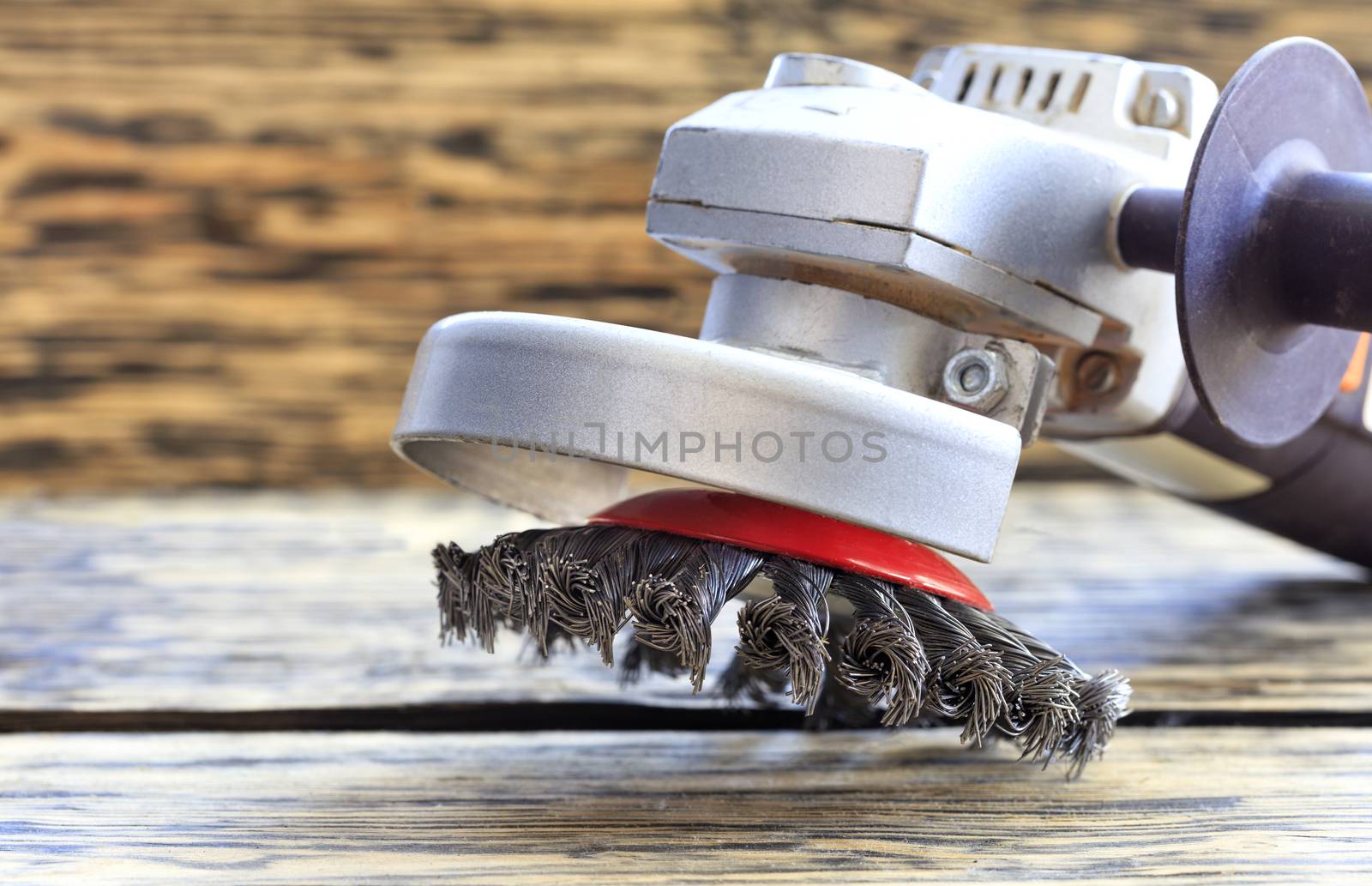 Angle grinder with abrasive wire brushes lies on the background of a wooden table.