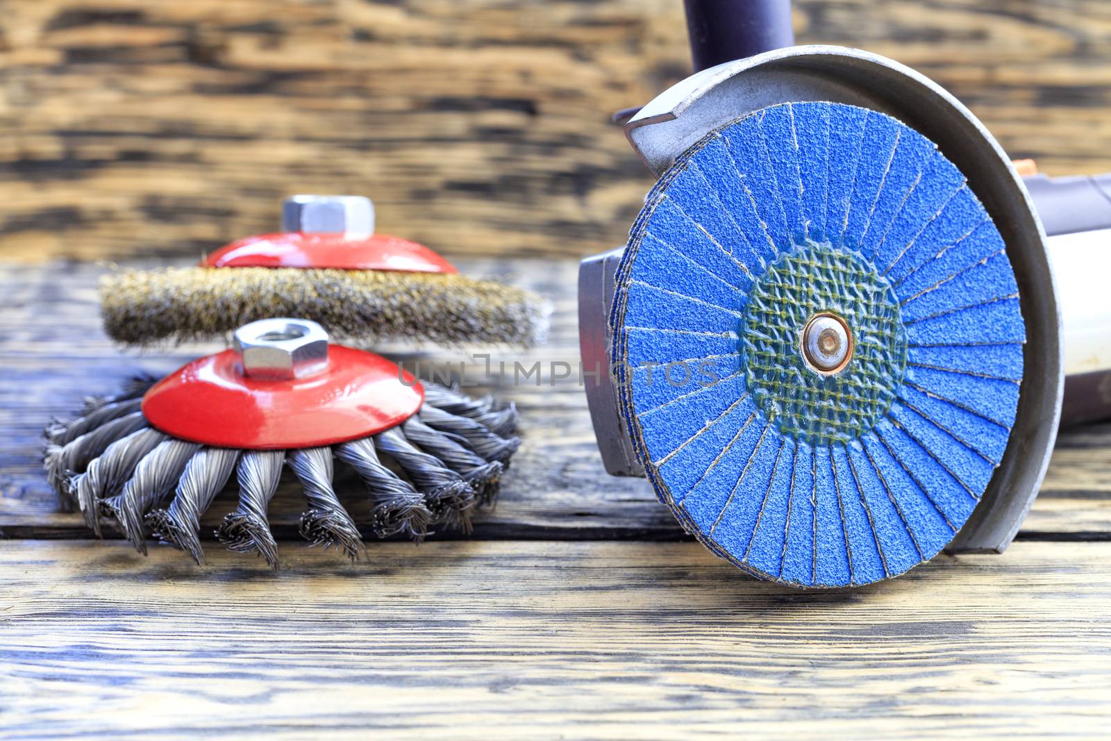 Angle grinder with grinding disc brushes and abrasive wire brushes lies on the background of a wooden table.