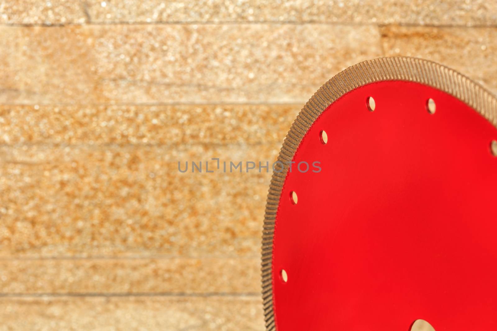 A fragment of a red diamond blade for cutting granite is turned toward the wall of golden sandstone. by Sergii