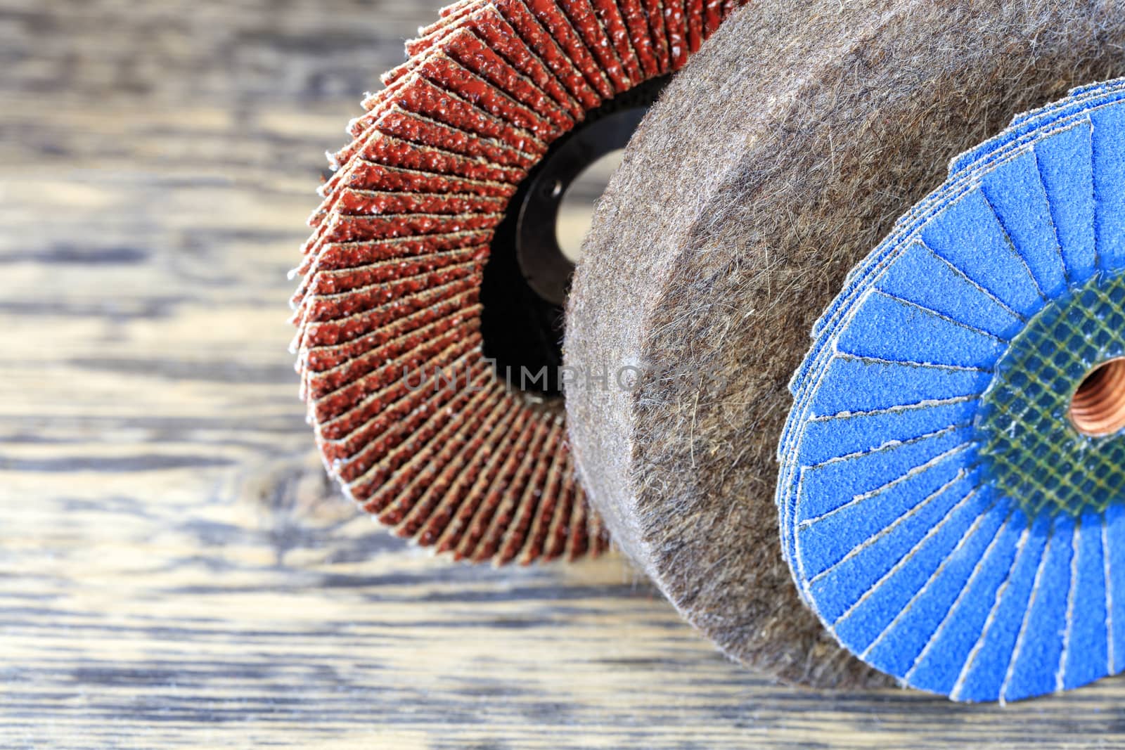 Part of the grinding wheels of various grains for grinding wood and rusty metal together with felt circle on a light beige background in unsharpness, close-up.