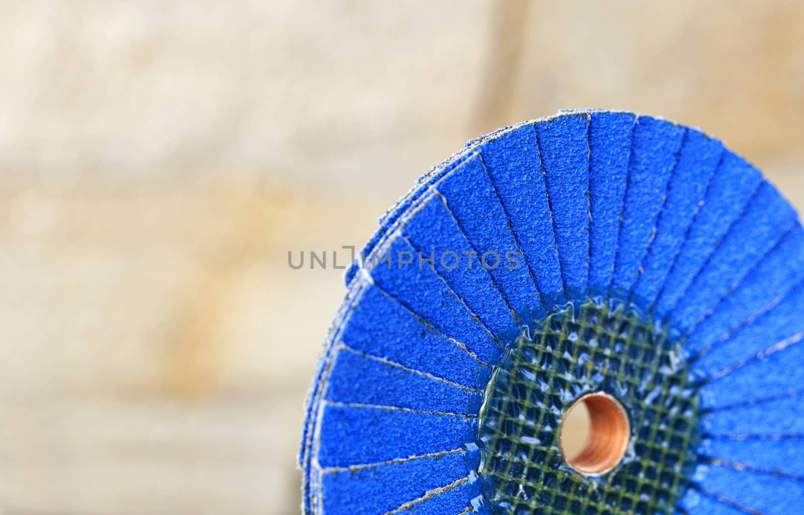 Flap grinding wheel blue on wood and metal on a light beige background in unsharp. by Sergii