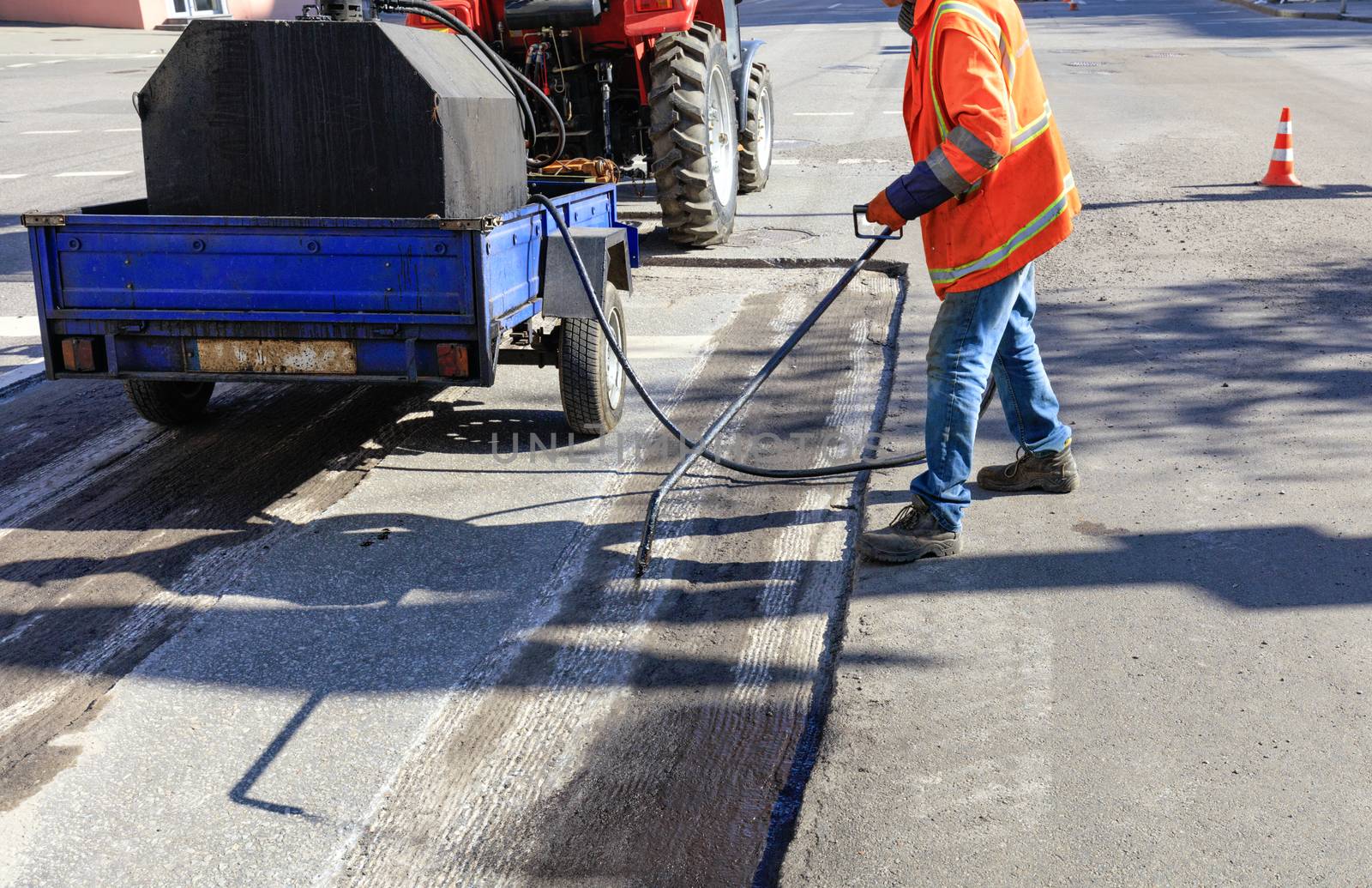 Worker repairs part of the asphalt road, spraying bitumen on the asphalt surface. by Sergii