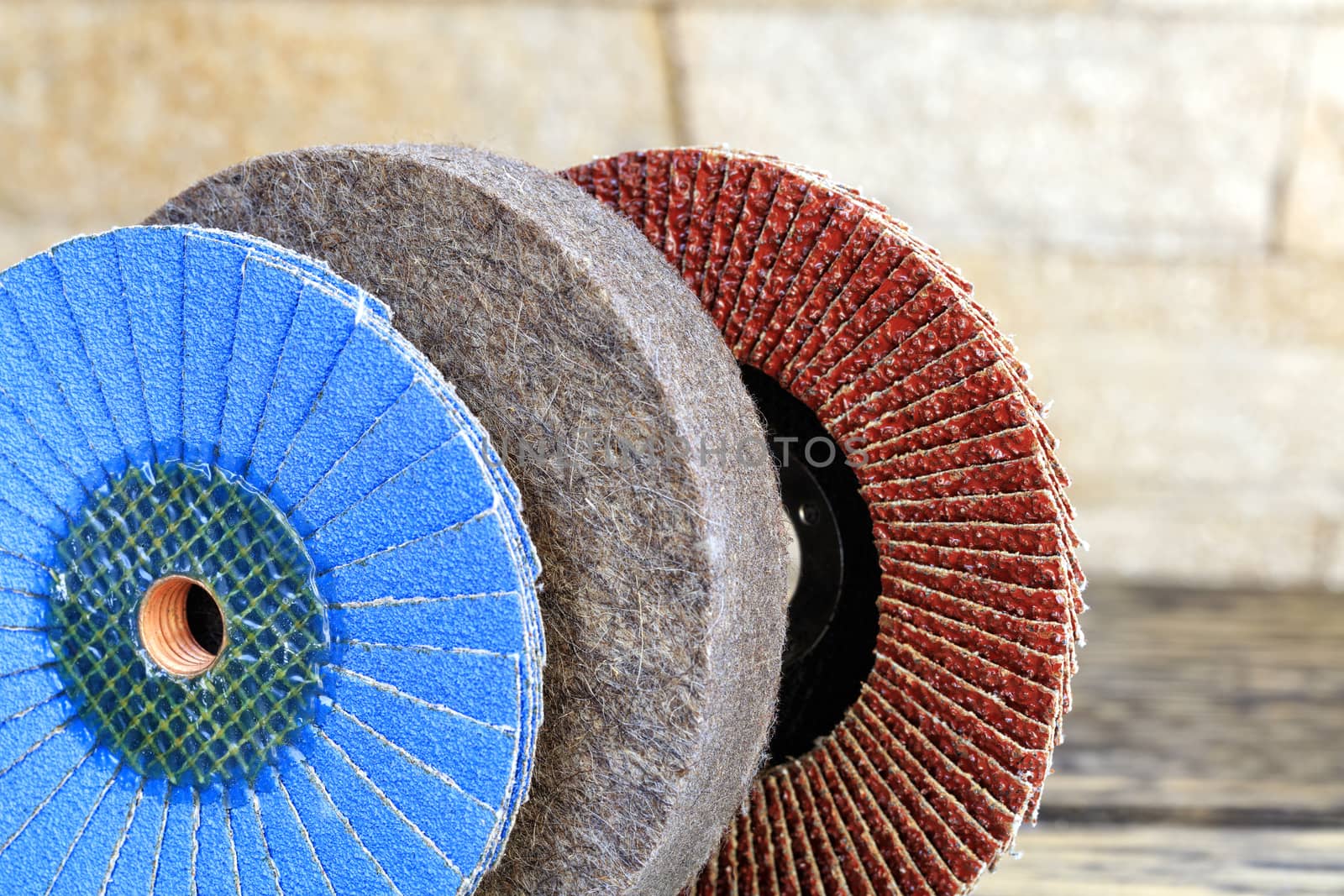 Grinding discs of various grains for grinding wood and rusty metal together with felt circle on a light beige background in unsharpness, close-up.