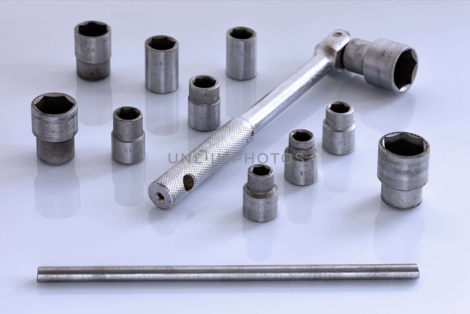 A universal set of tool heads with a ratchet for the car in on a glossy light gray background, close-up.